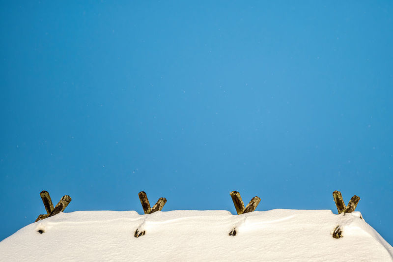 The roof ridge covered with snow with wooden decorative details against a blue sky, copy space
