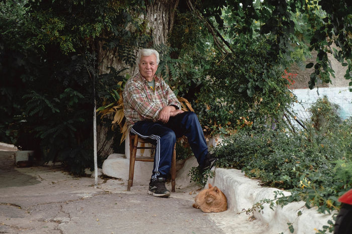 MAN WITH DOG SITTING ON CHAIR AGAINST TREES