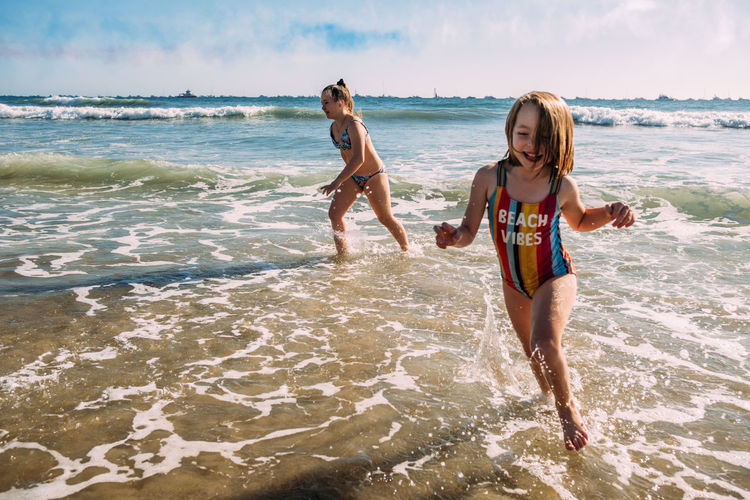 Sisters running on beach and splashing in water