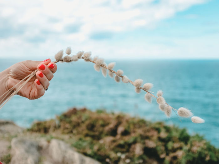 Close-up of hand holding rope over sea against sky