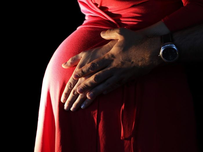 Cropped hand of man touching pregnant woman stomach against black background