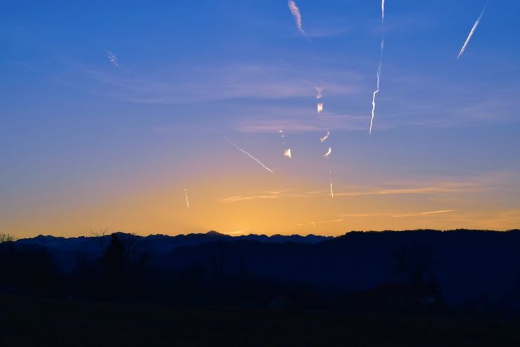 Silhouette landscape against vapor trails in sky during sunset