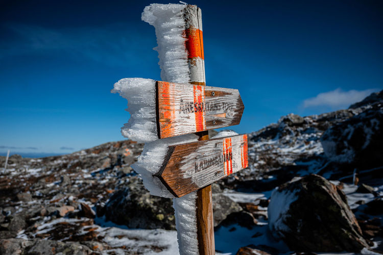 Close-up of sign board on snow covered mountain against blue sky