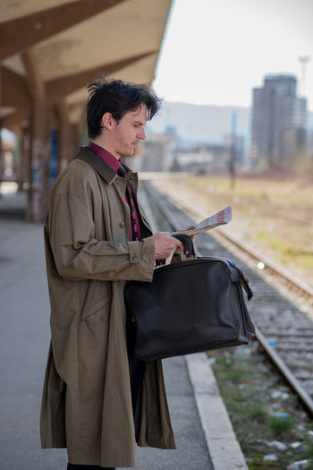 Side view of businessman reading newspaper while standing on platform