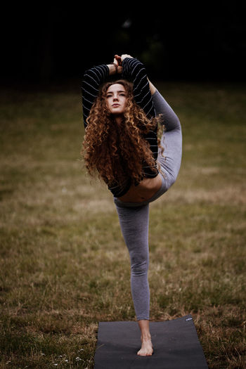 Full length of young woman standing on field on yoga matt 