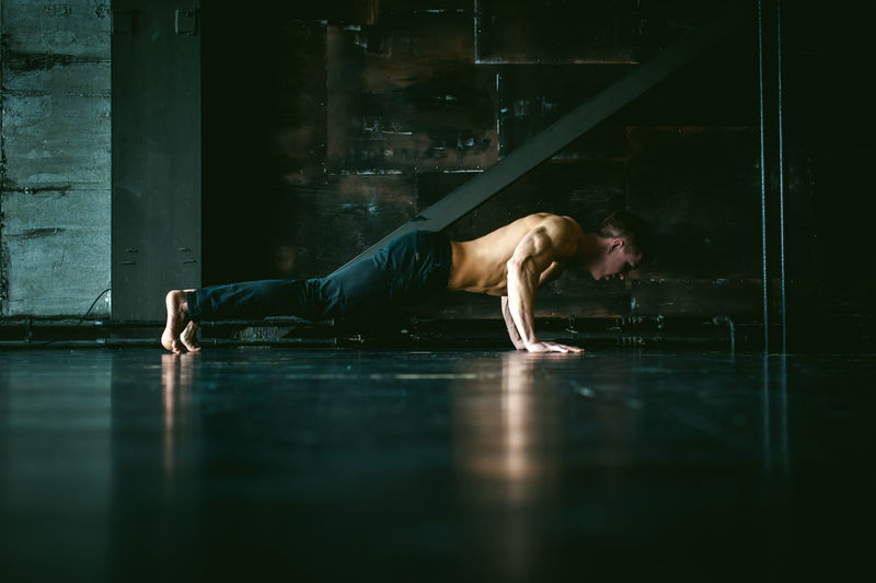 Shirtless muscular man practicing push-ups on floor