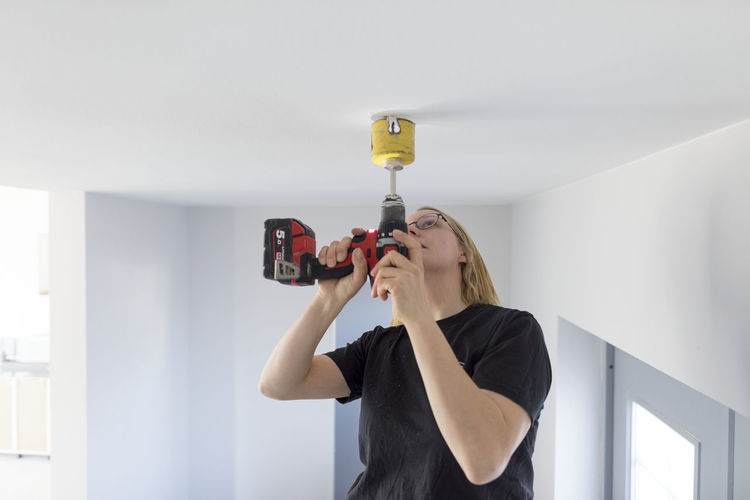 Man photographing woman standing against wall at home