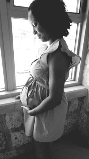 Side view of pregnant woman standing by window