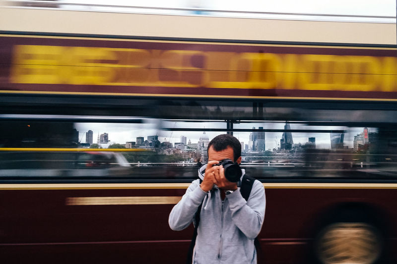 Man photographing against blurred motion of bus in city