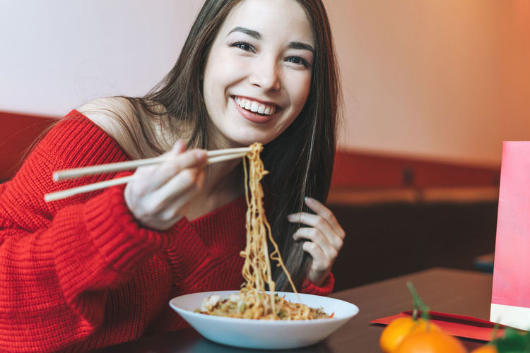 Asian woman in red clothes eating noodles with chopsticks in the chinese vietnamese restaurant