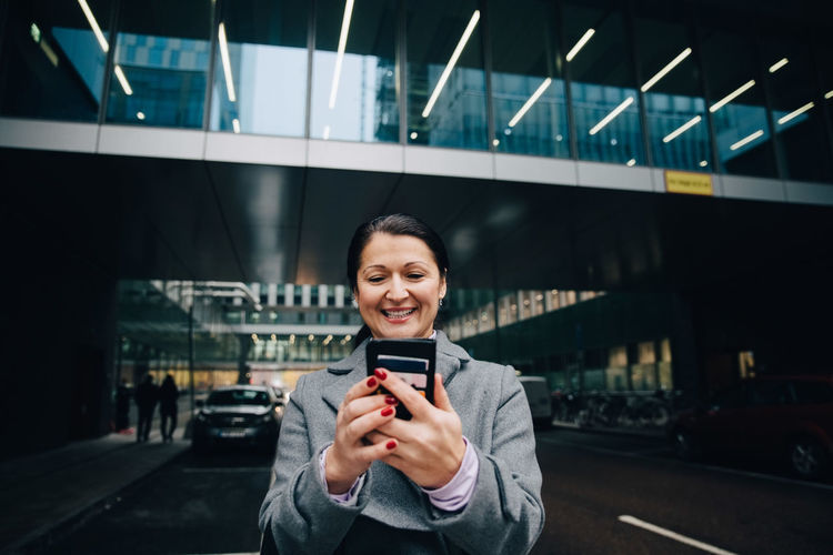 Portrait of smiling young woman using mobile phone while standing on bus
