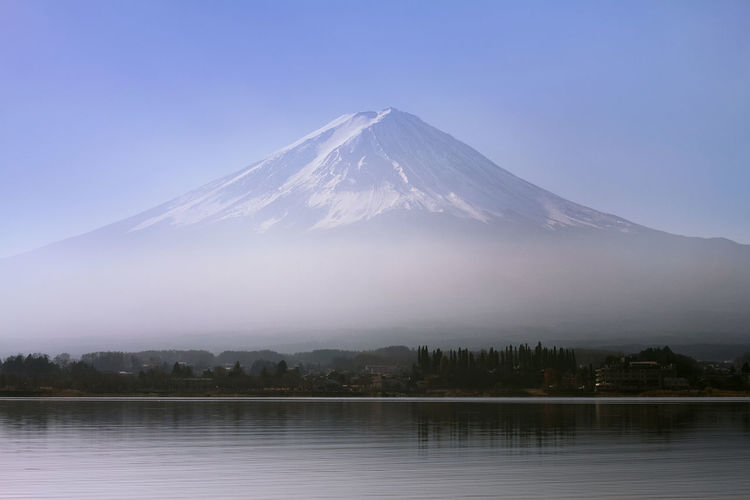 Scenic view of snowcapped mt fuji by against clear sky during foggy weather