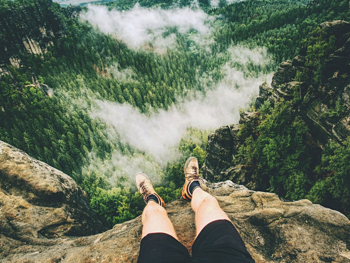 Guy relax on mountain top and enjoy view. feets in trekking shoes and legs short running trousers