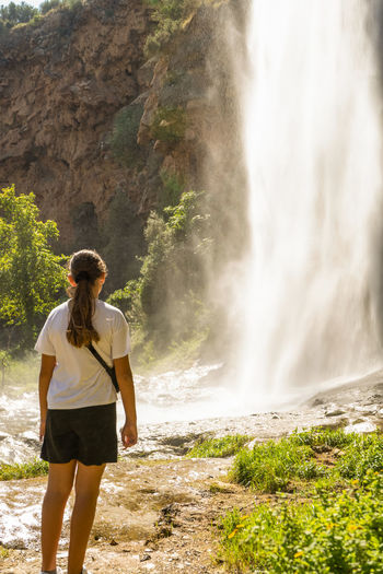 Full length of young woman standing against waterfall