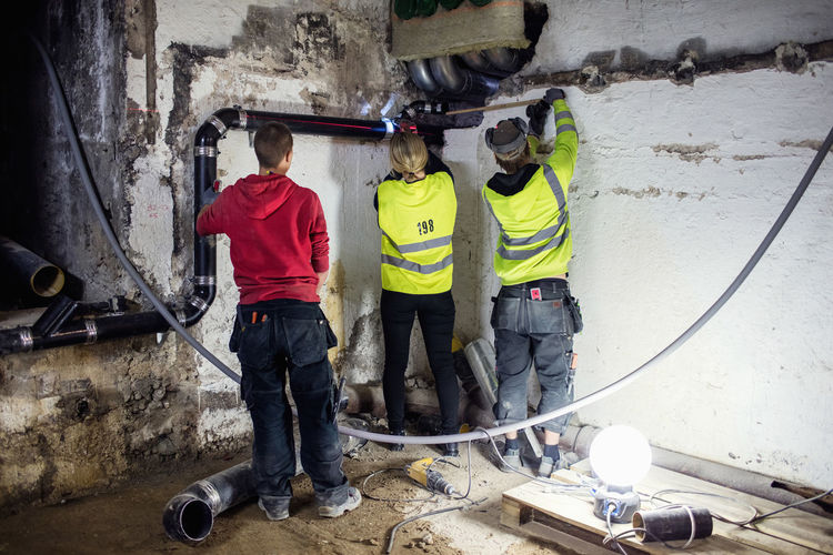 Rear view of plumbers repairing pipes in basement