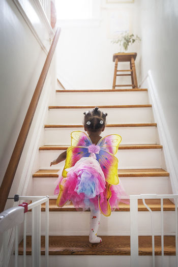 Rear view of girl dressed up in fairy costume moving up steps at home