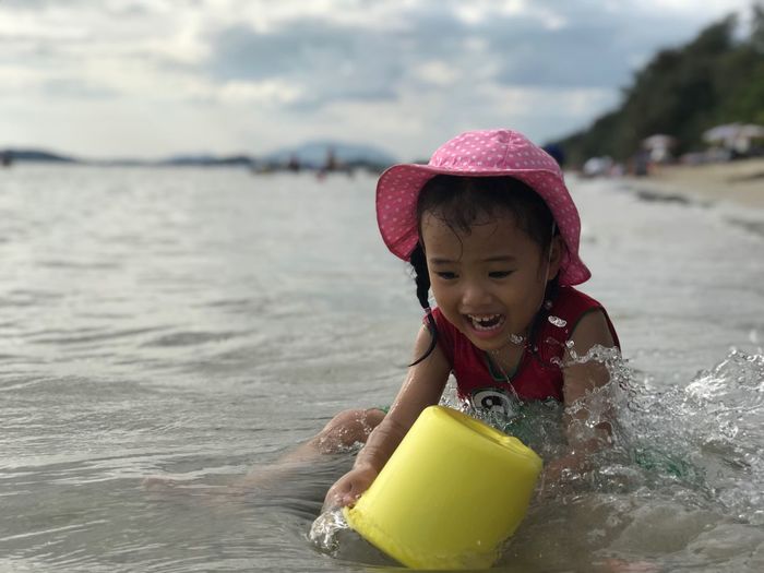 Girl playing with bucket while sitting at beach