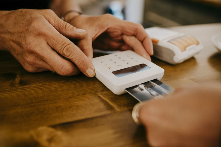 Cropped hand of customer paying owner through credit card at coffee shop