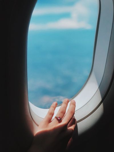 CROPPED IMAGE OF HAND BY AIRPLANE WINDOW