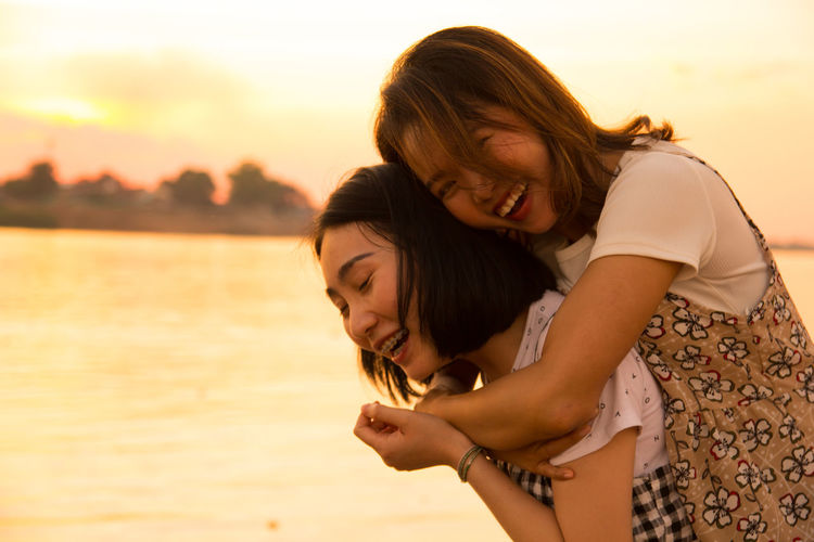 Woman piggybacking friend against sky during sunset