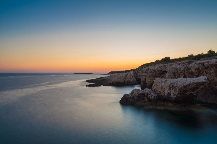 Scenic view of rock formation and sea against sky during sunset