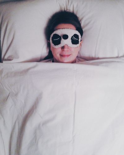 High angle view of smiling woman wearing sleep mask while resting on bed
