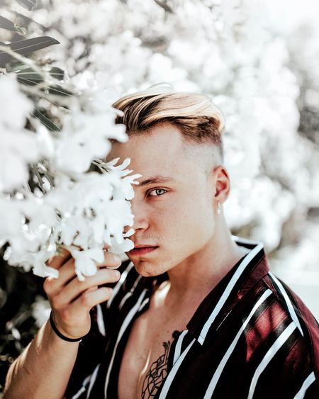 Portrait of young man smelling white flowers