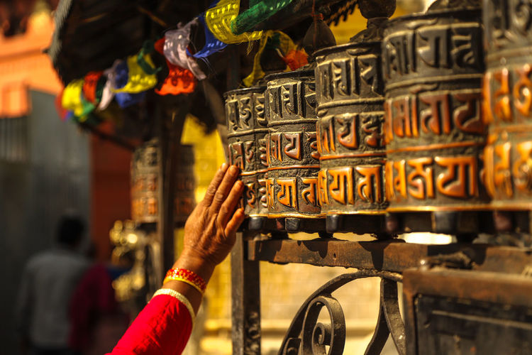 Cropped image of woman touching prayer wheels in temple