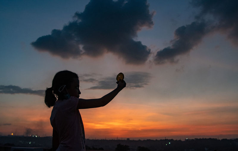 Silhouette of girl standing against sky during sunset