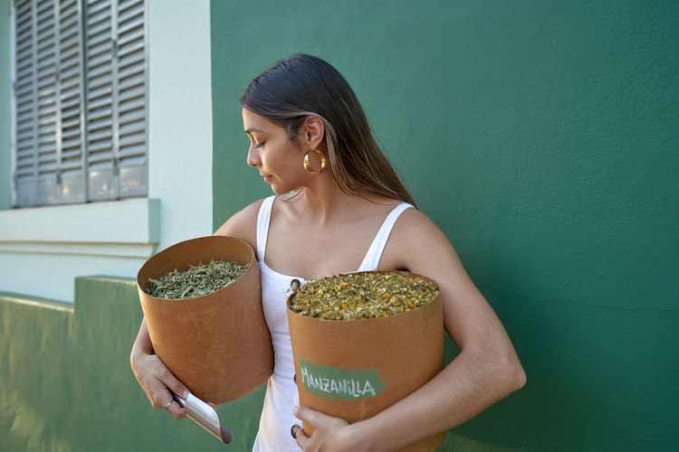 Woman holding container with dried herbal chamomile ginger tea.