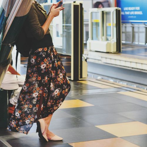 Low section of woman using mobile phone on railroad station platform