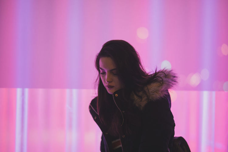 Thoughtful young woman standing against pink light at night