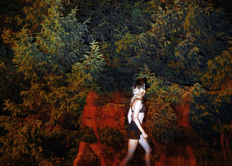 Multiple exposure image of woman walking by tree in forest