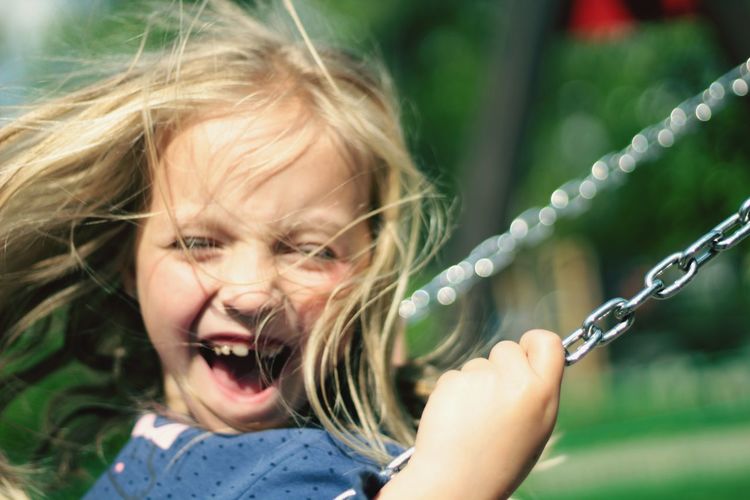 Close-up of cheerful girl with blond hair enjoying swing
