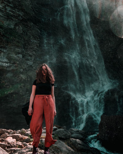 Portrait of woman standing on rock against waterfall