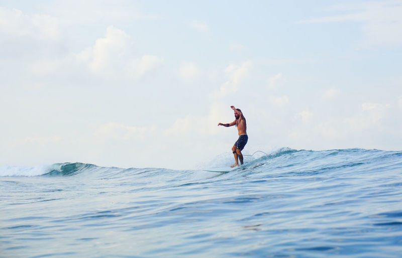 Young man surfing on sea against sky