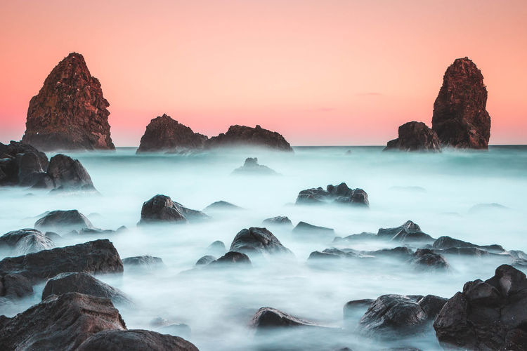 Rocks in sea against sky during sunset