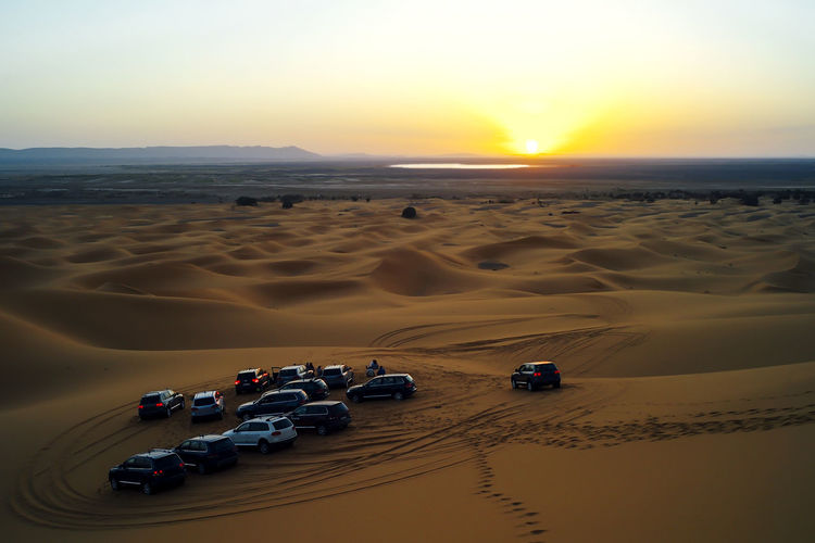 People watch the sunset in the moroccan desert from their 4x4 cars