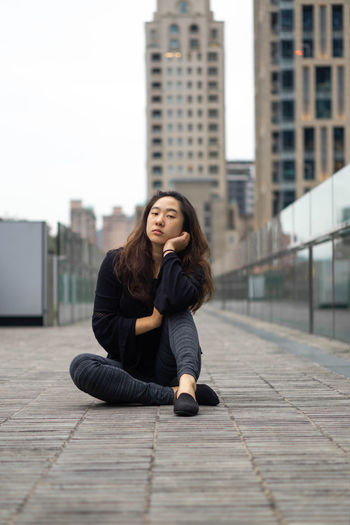 Portrait of young woman sitting on sidewalk in city