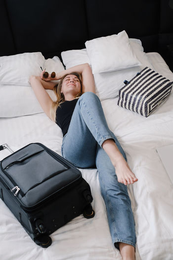 Woman with suitcase on bed in hotel having rest while traveling traveler with bag arriving at resort