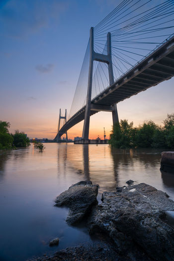 Low angle view of suspension bridge over river during sunset