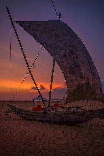 Old sailboat moored at beach against sky during sunset