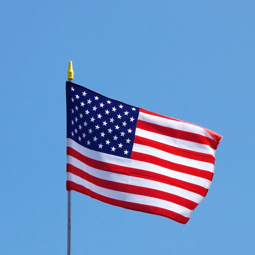 Low angle view of american flag waving against clear blue sky during sunny day