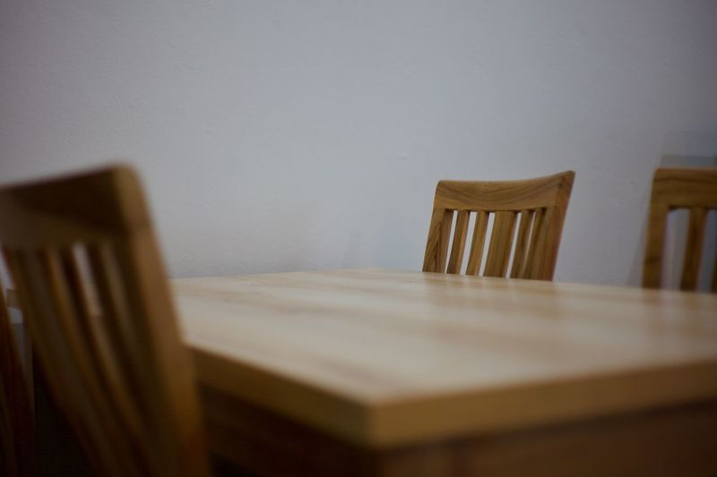 Empty wooden table amidst chairs by white wall