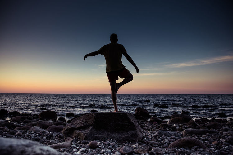 Full length of man exercising at beach against sky during sunset