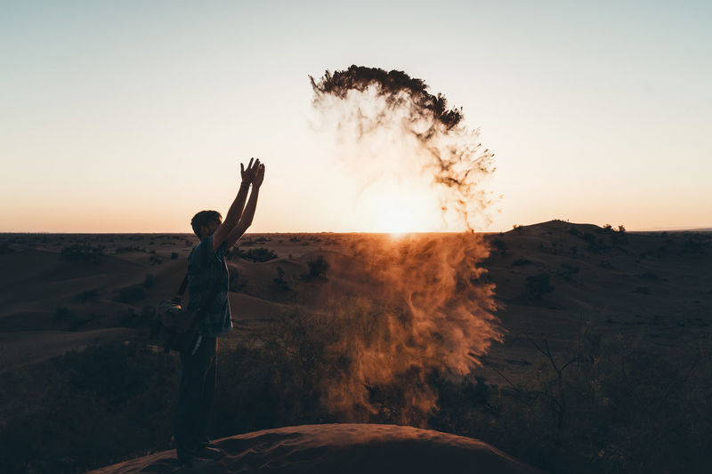 Side view of man throwing sand at desert against clear sky