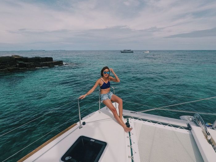Woman in sunglasses relaxing in yacht on sea against cloudy sky