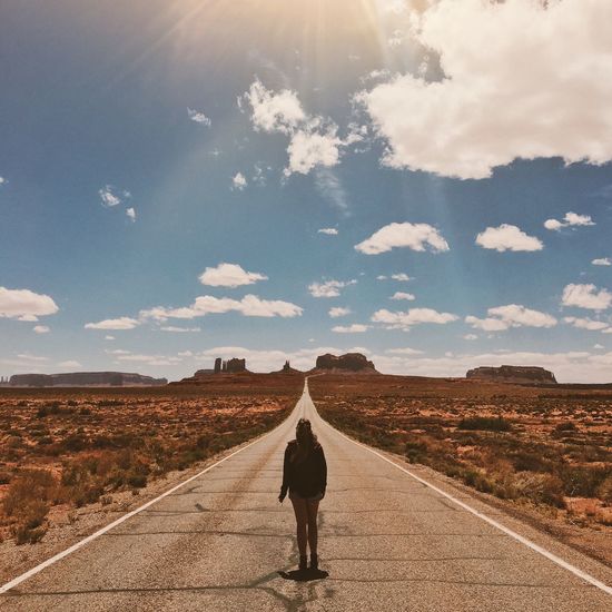 Rear view of woman standing on country road against sky at monument valley