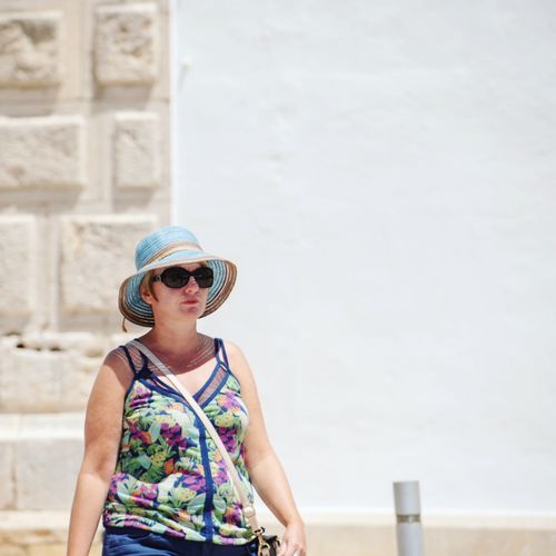 Woman wearing sunglasses and hat while standing against wall