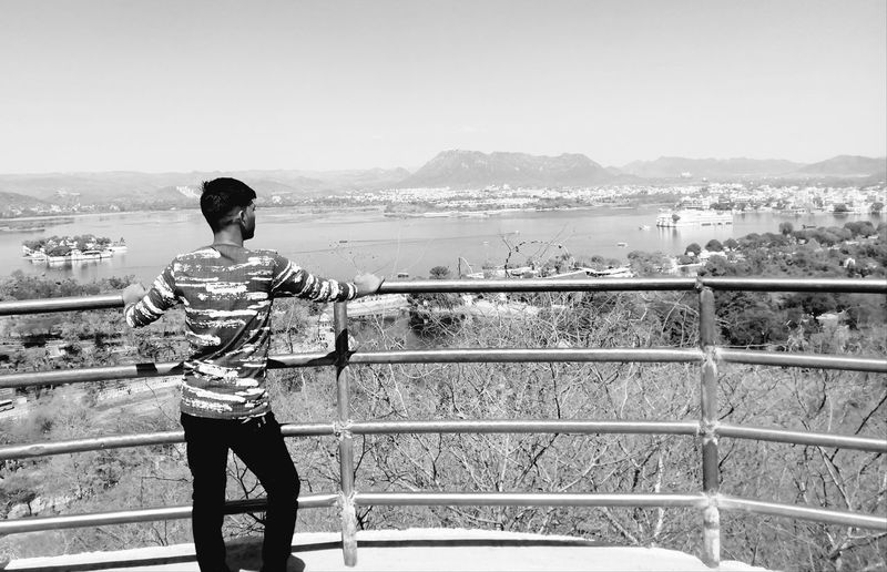 Rear view of man standing by railing against sky